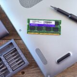 Laptop deschis pe un birou de service, cu un SSD nou pregătit pentru montare