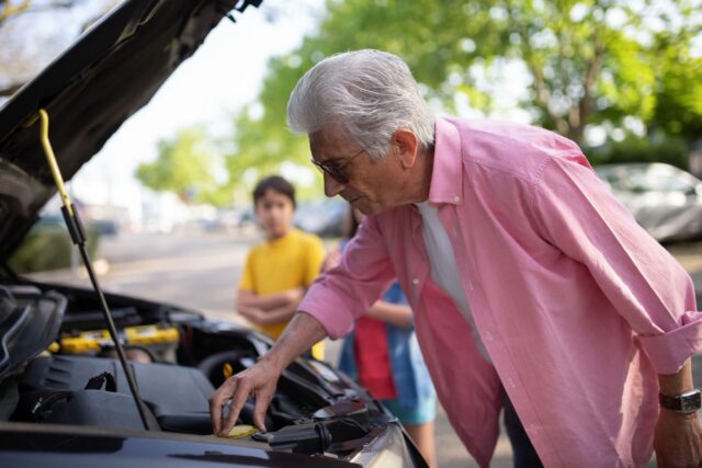 Bărbat care inspectează compartimentul motor al unei mașini second-hand cu capota ridicată
