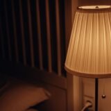 Dormitor liniștit, cu lenjerie albă și o veioză cu lumină caldă aprinsă pe noptieră